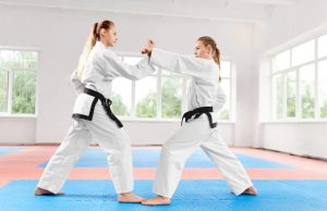 Two women practicing karate in a dojo with blue and red mat