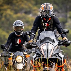 Two motorcyclists with helmets riding through a field