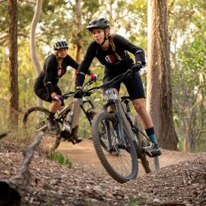 Two mountain bikers navigating a trail through a forested area.