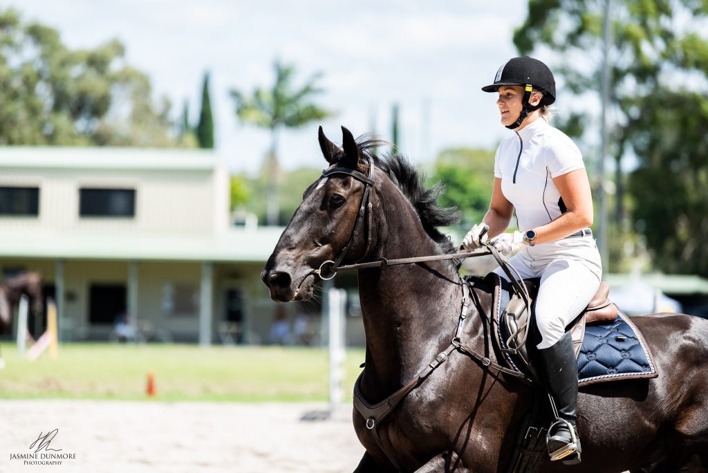 equestrian rider in white attire and helmet riding a dark horse with focused expression during training