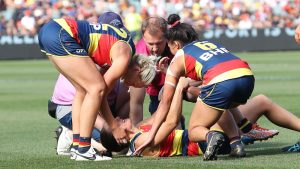 Female athletes and a trainer attending to an injured player during an Australian rules football match.