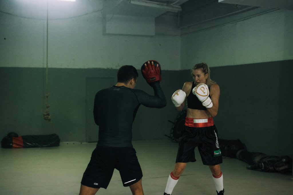 a female boxer training with a male coach in a dimly lit gym both wearing boxing gloves and focused on the exercise