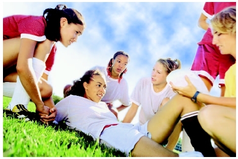 young female soccer player lying on the grass with teammates and coach gathered around her