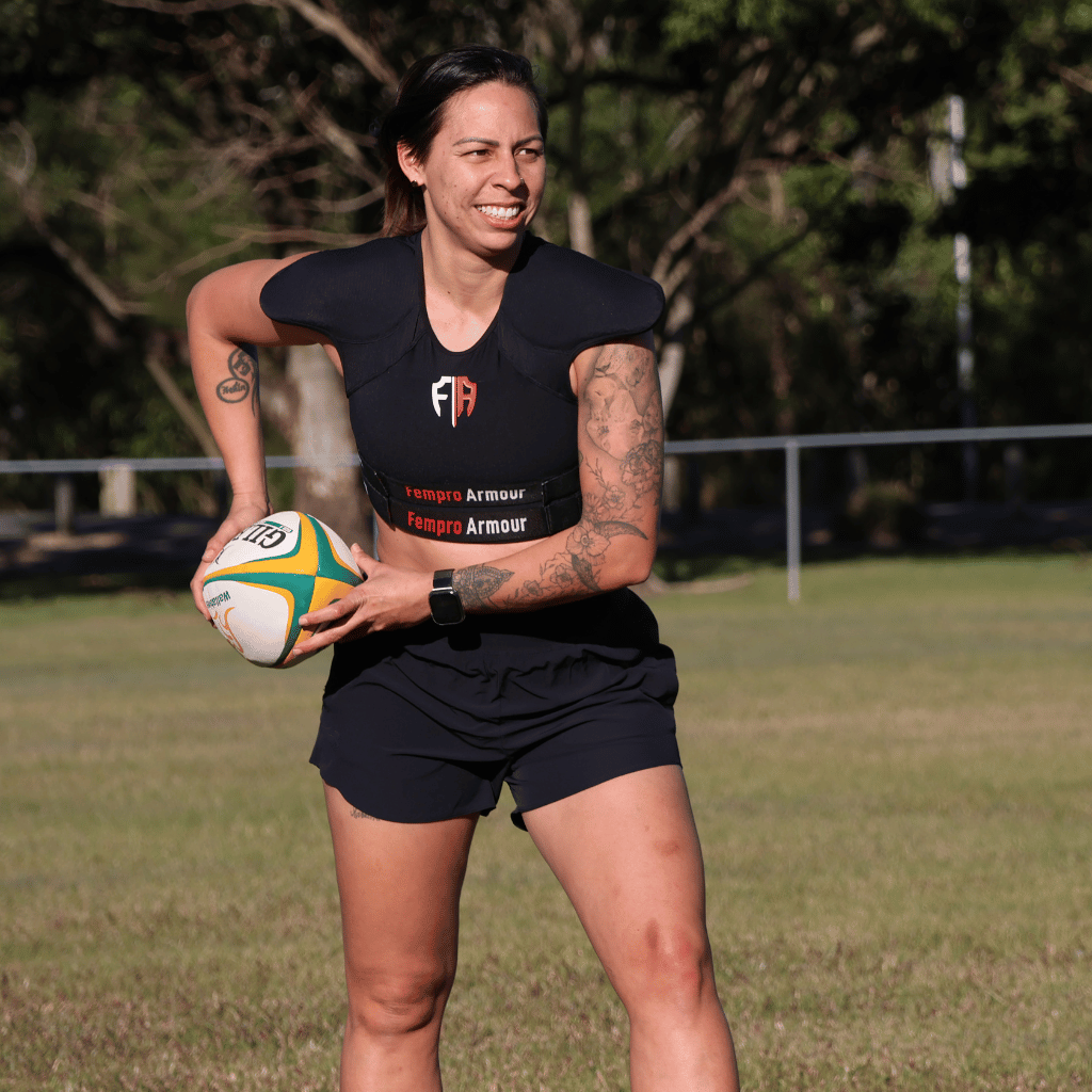 Female rugby player wearing Fempro Armour gear holding a rugby ball on a field.